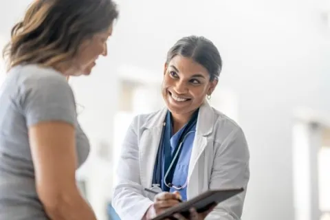 A smiling NP shows a patient a tablet.