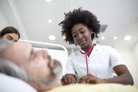 A nurse practitioner checks a patient’s vital signs in the hospital room.